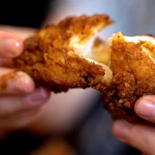 a hand holding a piece of fried chicken