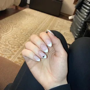 White French tip acrylic nails with small black heart on ring finger