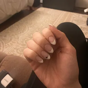 White French tip acrylic nails with small black heart on ring finger