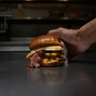 a hand holding a bacon and egg sandwich