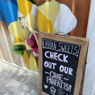 Chalkboard announcement framed by a mural on the side of the shipping container