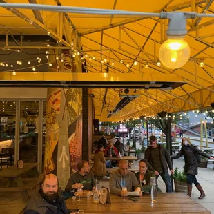 a group of people sitting at tables under a yellow awning