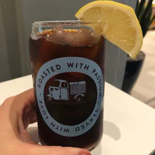 a hand holding a glass of iced tea with a lemon wedge