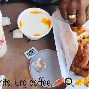 Breakfast sandwich on croissant with scrambled eggs, cheddar, bacon. Side of creamy grits with cheese and a large coffee