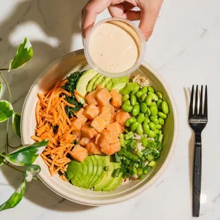 a person pouring dressing on a bowl of vegetables