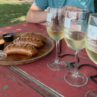 a man sitting at a picnic table with a plate of pretzels and two glasses of wine