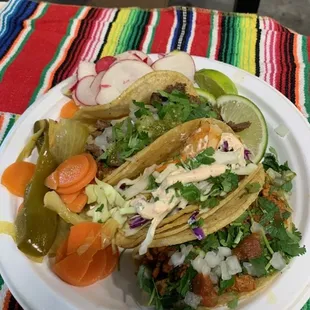 A colorful plate of tacos topped with fresh cilantro, onions, and slaw, paired with pickled veggies and lime for a burst of flavor!