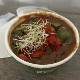 a bowl of soup with tomatoes and sprouts