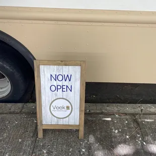 a now open sign on a sidewalk