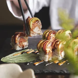 a person holding chopsticks over a sushi