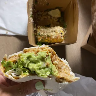 a hand holding a burrito with guacamole