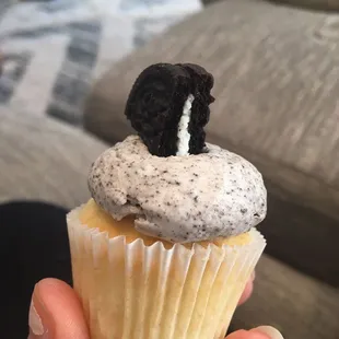 a person holding a cupcake with ore cookies on top