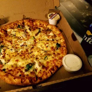 A white pizza with broccoli, onions, tomatoes and mushrooms as toppings, and ranch and garlic sauce on side.