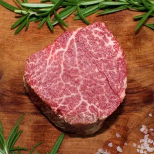 a steak on a cutting board with rosemary sprigs