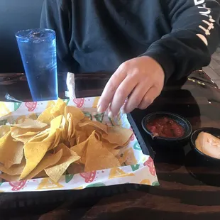 a person sitting at a table with a tray of chips and dips