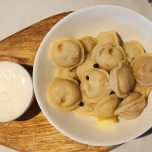 a bowl of tortelli with a side of sour cream