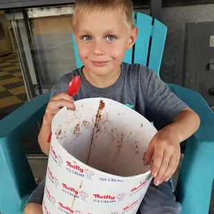 a young boy sitting in a chair holding a bucket of ice cream