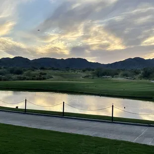 a golf course with a pond and mountains in the background