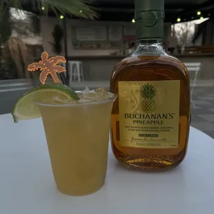 a bottle of buchanan's pineapple syrup and a glass with a lime wedge