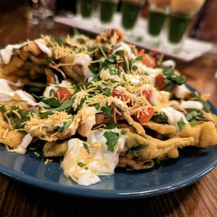 Palak Chaat. $12. Crispy chickpea-battered spinach topped with onion, tomato, yogurt, and house chutneys.