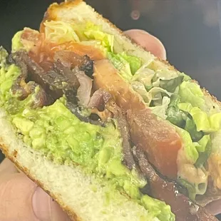 a hand holding a sandwich with meat and lettuce