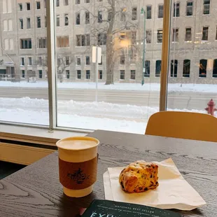 a cup of coffee and a pastry on a table in front of a window