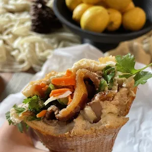 a person holding a sandwich with meat and vegetables