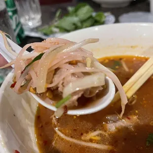 a person holding chopsticks over a bowl of soup