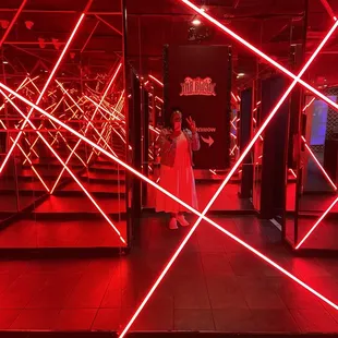 a woman in a red dress standing in front of a line of red laser lights