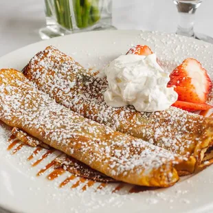 a plate of crepes with strawberries and whipped cream