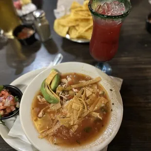 a bowl of soup with tortilla, avocado, and salsa
