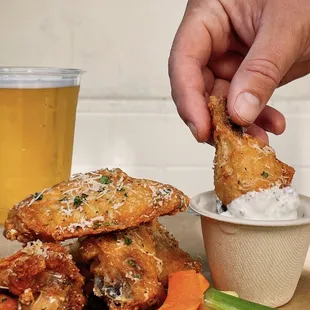 a hand dipping a piece of chicken wings