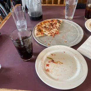 Mostly eaten pizza with bacon and spinach toppings, along with a carafe of soda.