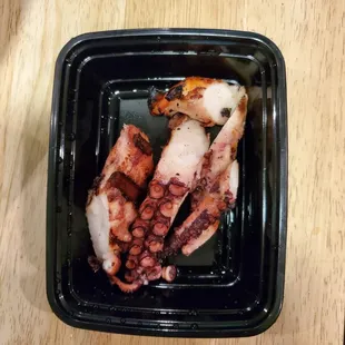 a black plastic container with cooked octopus
