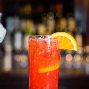 a red drink with a slice of orange