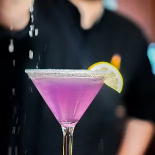 a bartender pouring a purple cocktail