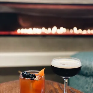 two cocktails on a table in front of a fireplace