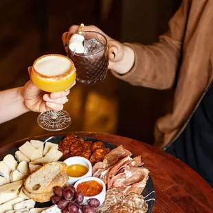 two people toasting glasses of wine over a platter of appetizers