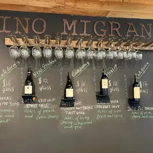 a wall of wine glasses and a chalk board