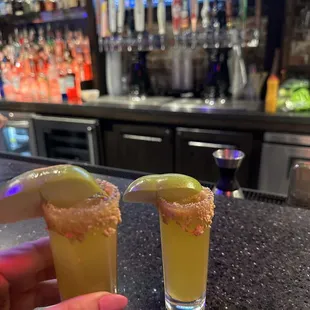 two margaritas with lime wedges on a bar counter