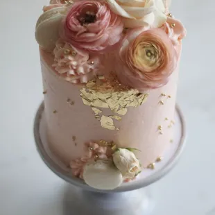 a pink and gold cake with flowers on top