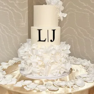 Elegant 3 tiered wedding cake with ruffled petals on lower tier, monogrammed middle tier, sugar flowers topper