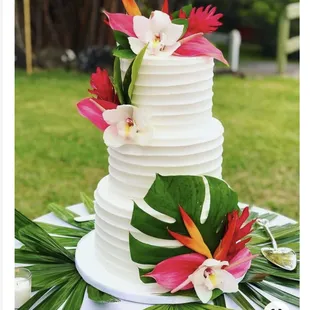 3 tiered white wedding cake with tropical pink flowers and green leaves