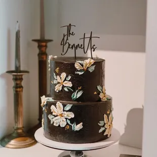 Black wedding cake with ivory palette knife flower, gold centers and green leaves