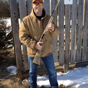a man holding a shotgun in front of a fence