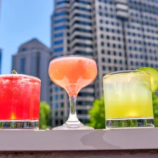 three cocktails on a rooftop overlooking a cityscape