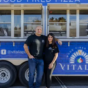 a man and woman standing in front of a food truck