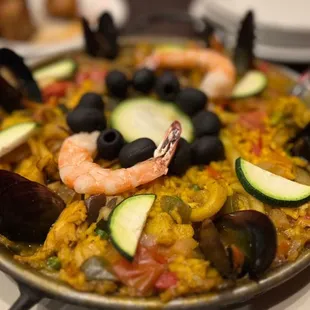 a plate of paella with shrimp, zucchini and olives