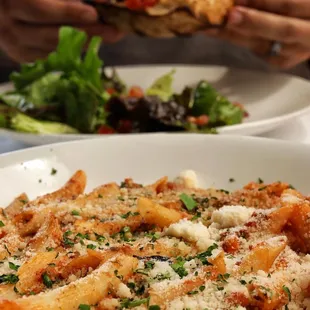 a plate of pasta with a burger in the background