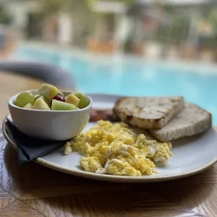 a plate of eggs, bread and a bowl of fruit